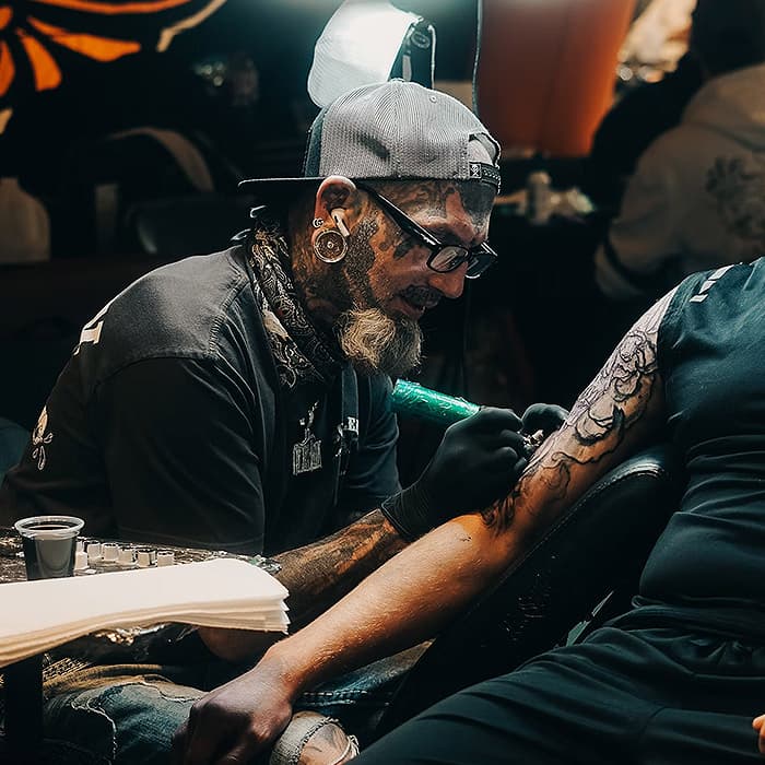 A tattoo shop owner working on a tattoo on the arm of a customer